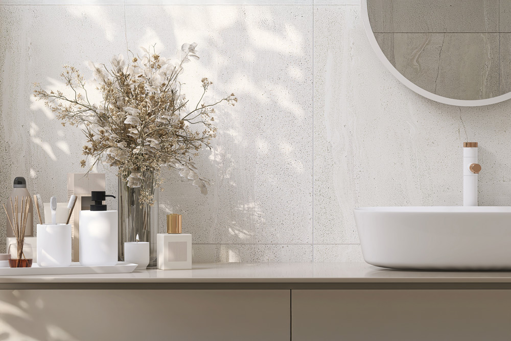 Ljust badrum med vit handfatsskål, rund spegel och dekorativa torkade blommor i vas